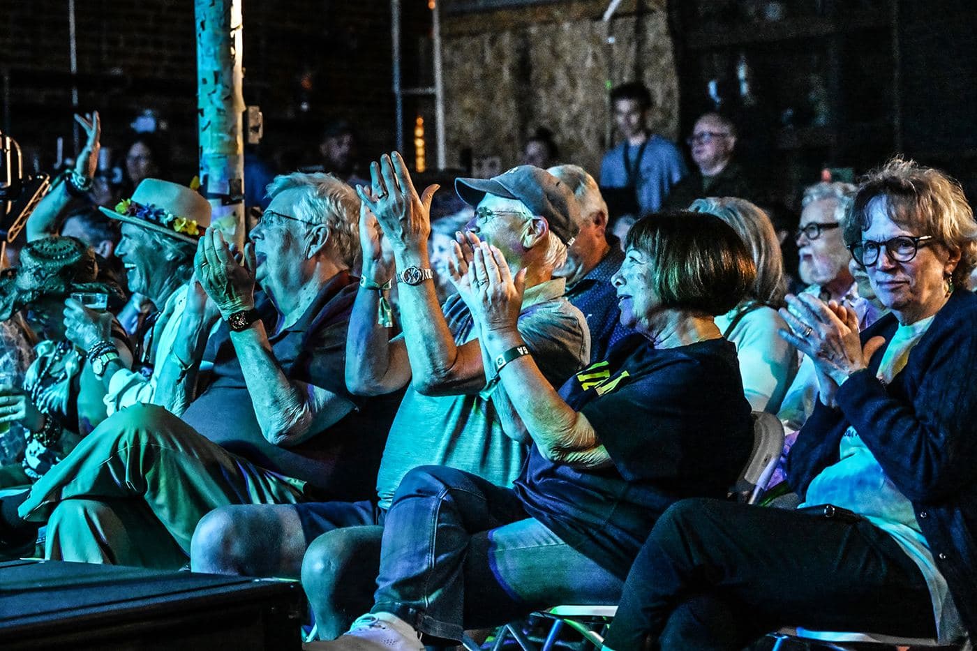A packed audience applauding in teal stage light at the end of a set