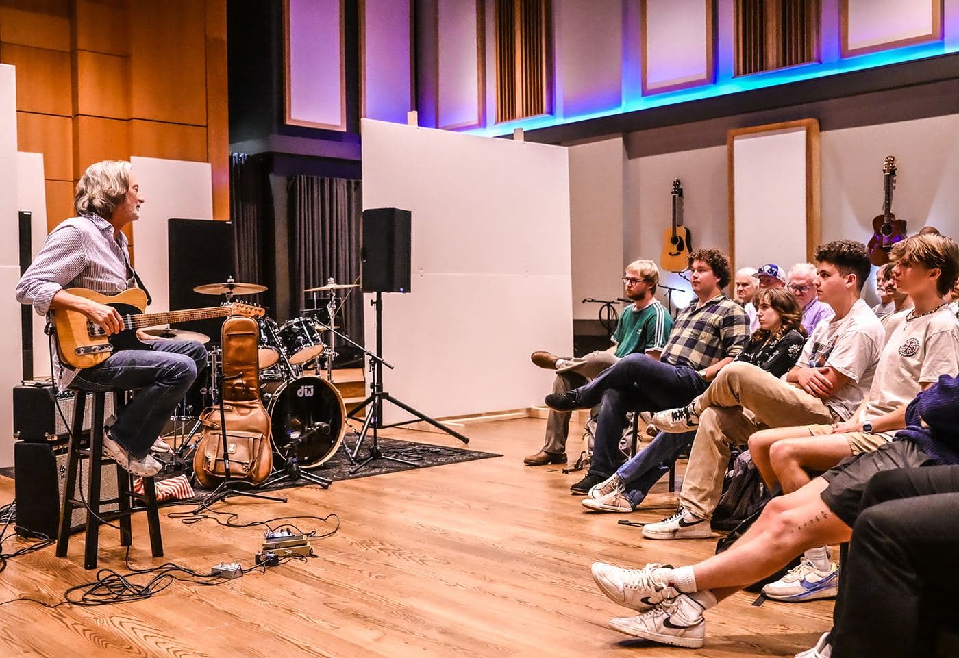 A guitarist teaching a room of seated students at a hands-on festival workshop