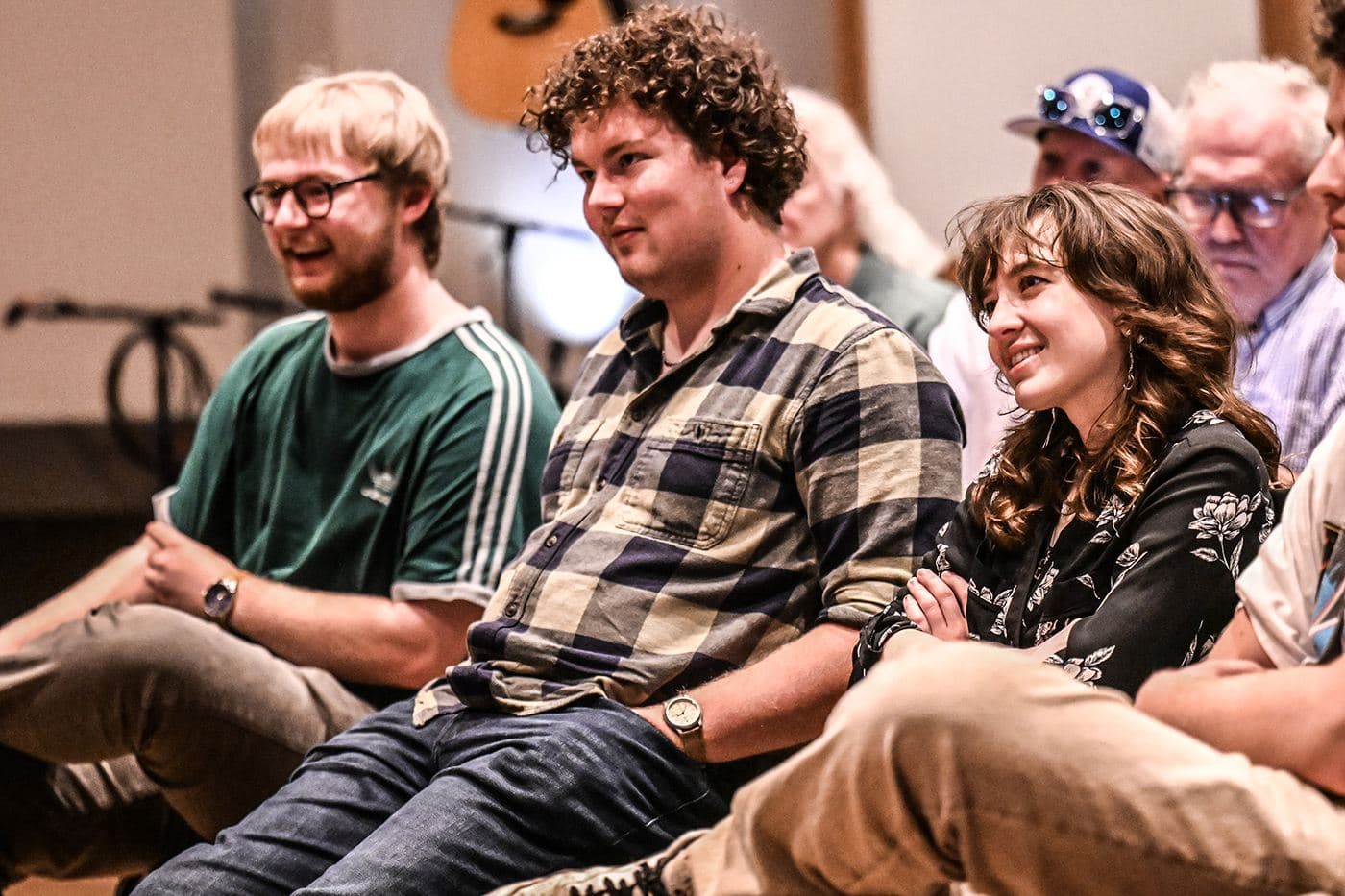 Students listening close up during a festival masterclass, guitars racked on the wall behind them